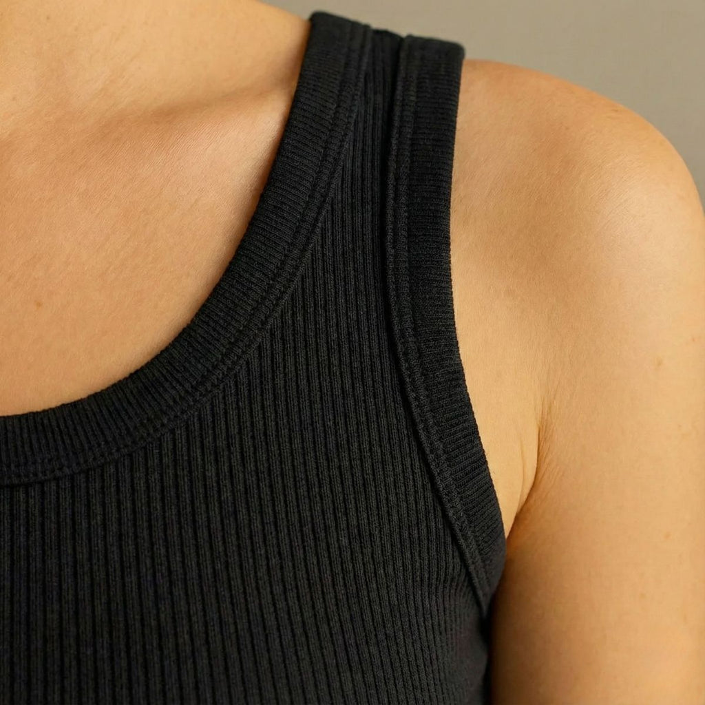 Close-up of a person wearing a black ribbed tank top against a neutral background