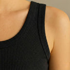 Close-up of a person wearing a black ribbed tank top against a neutral background