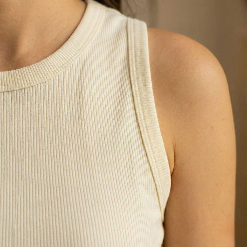 Close-up of a person wearing a beige ribbed tank top against a neutral background