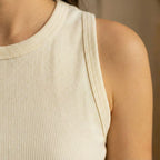 Close-up of a person wearing a beige ribbed tank top against a neutral background