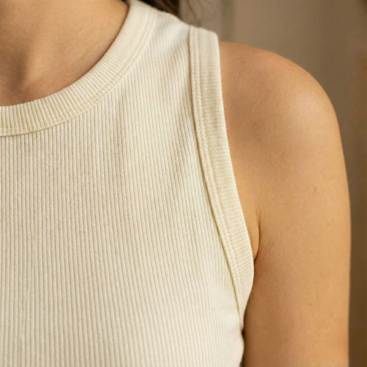 Close-up of a person wearing a beige ribbed tank top against a neutral background