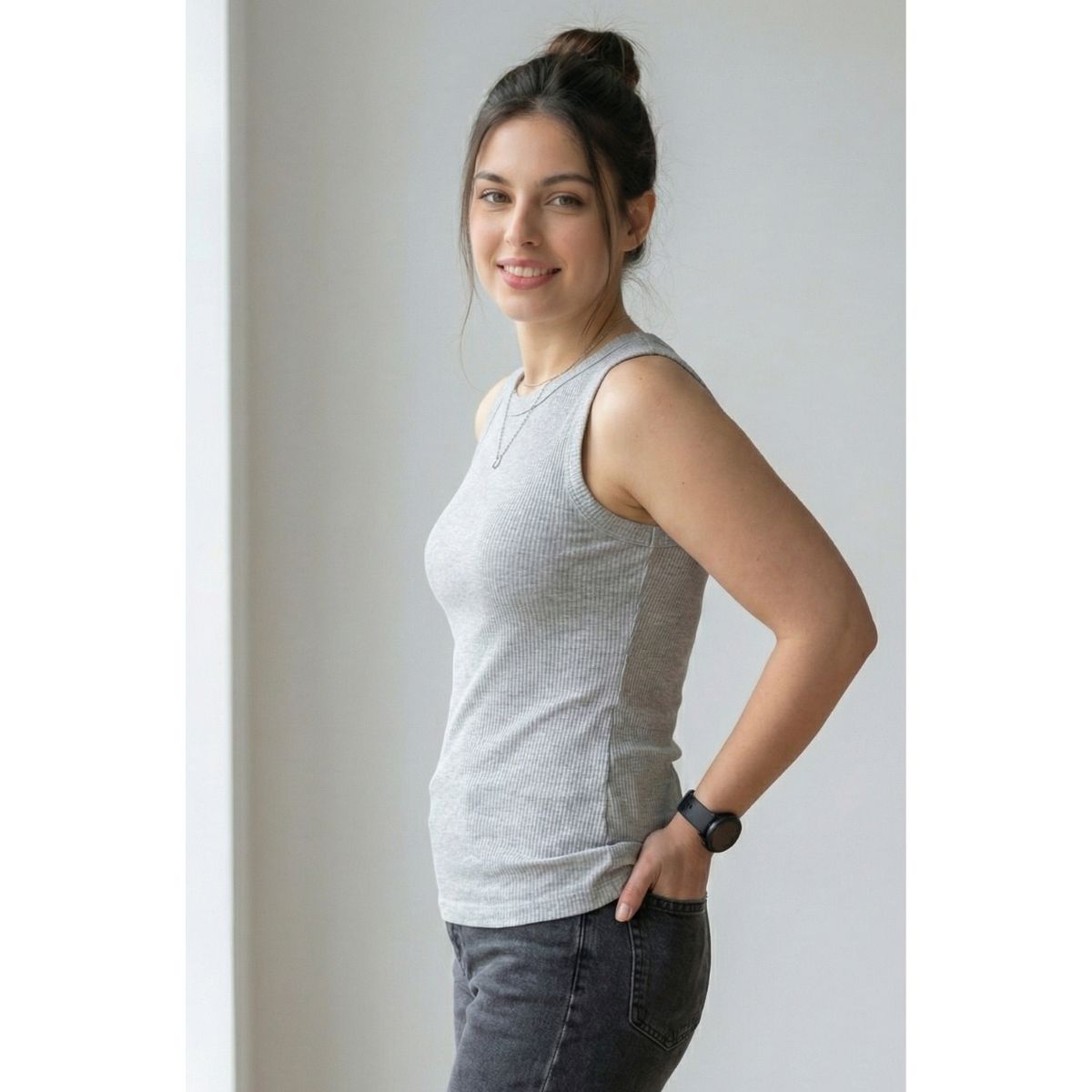 Woman wearing a gray sleeveless top and dark pants against a plain background