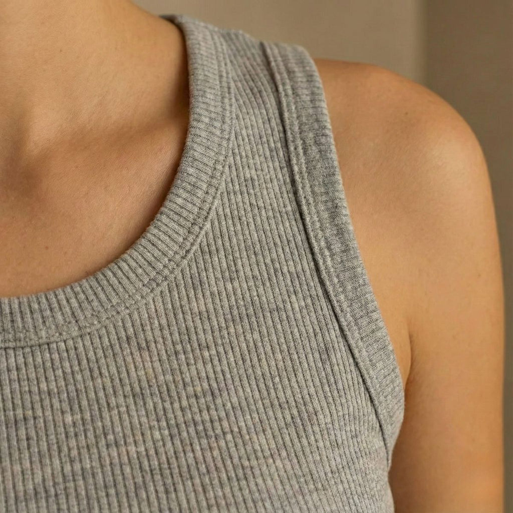 Close-up of a person wearing a gray ribbed tank top against a neutral background
