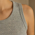 Close-up of a person wearing a gray ribbed tank top against a neutral background