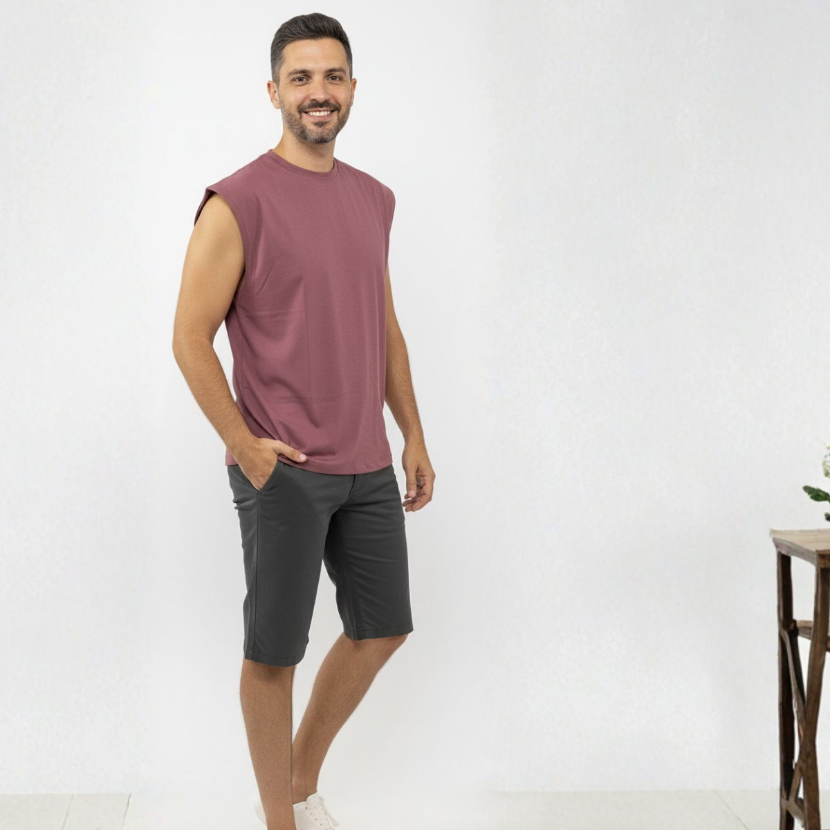 Man wearing a sleeveless rosé tank top shirt and black shorts on a white background